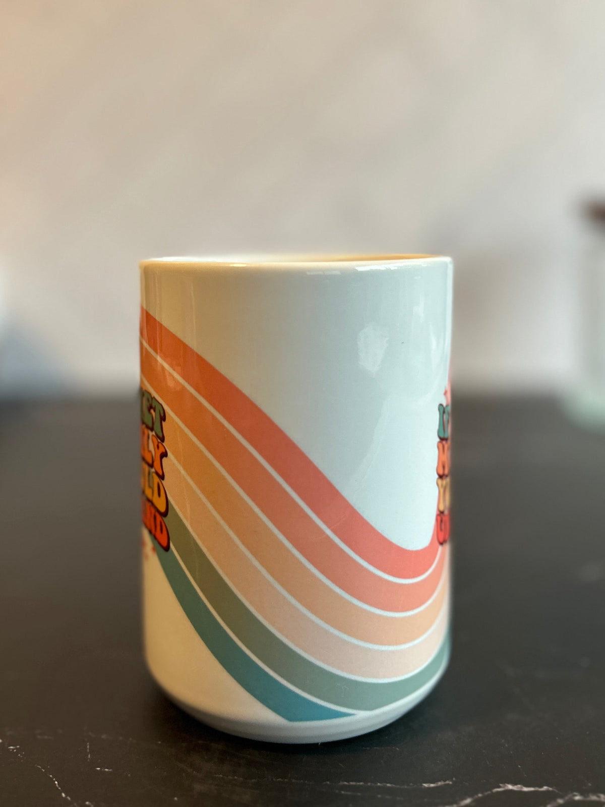 A white ceramic mug with retro wavy stripes in orange, pink, and teal, sitting on a dark marble countertop with a blurred background.