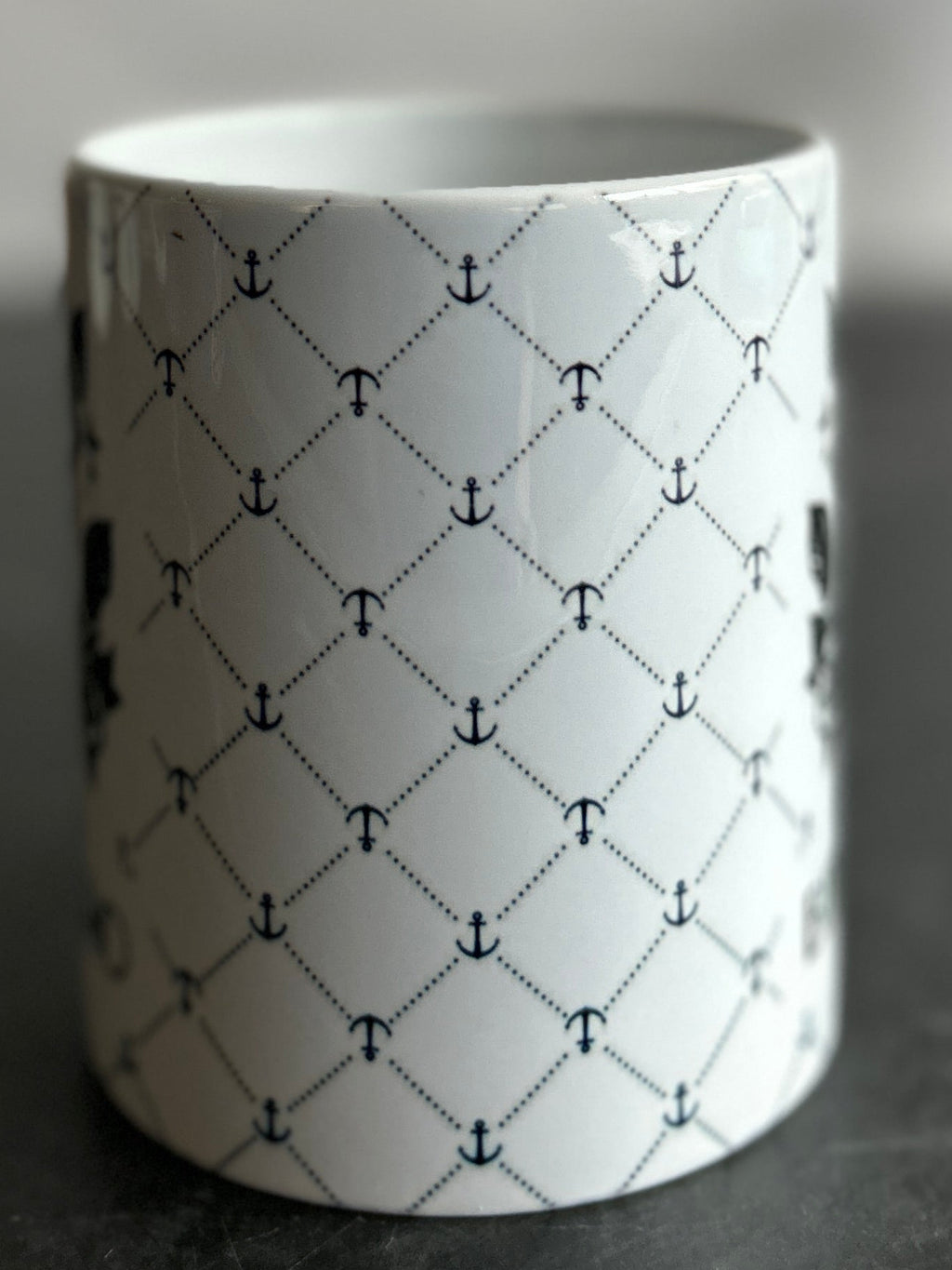 A white ceramic mug with a black geometric lattice pattern, standing on a dark marble surface against a blurred gray background.